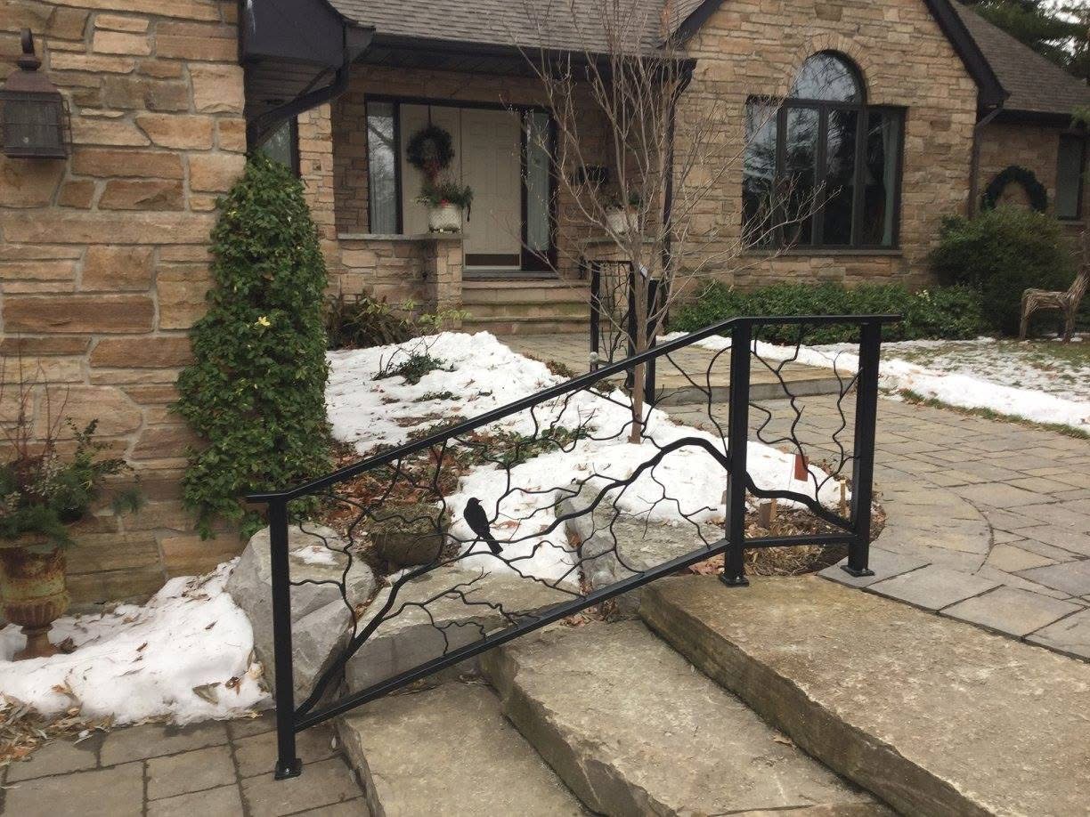 Decorative black metal railing with branch silhouette outside a stone house