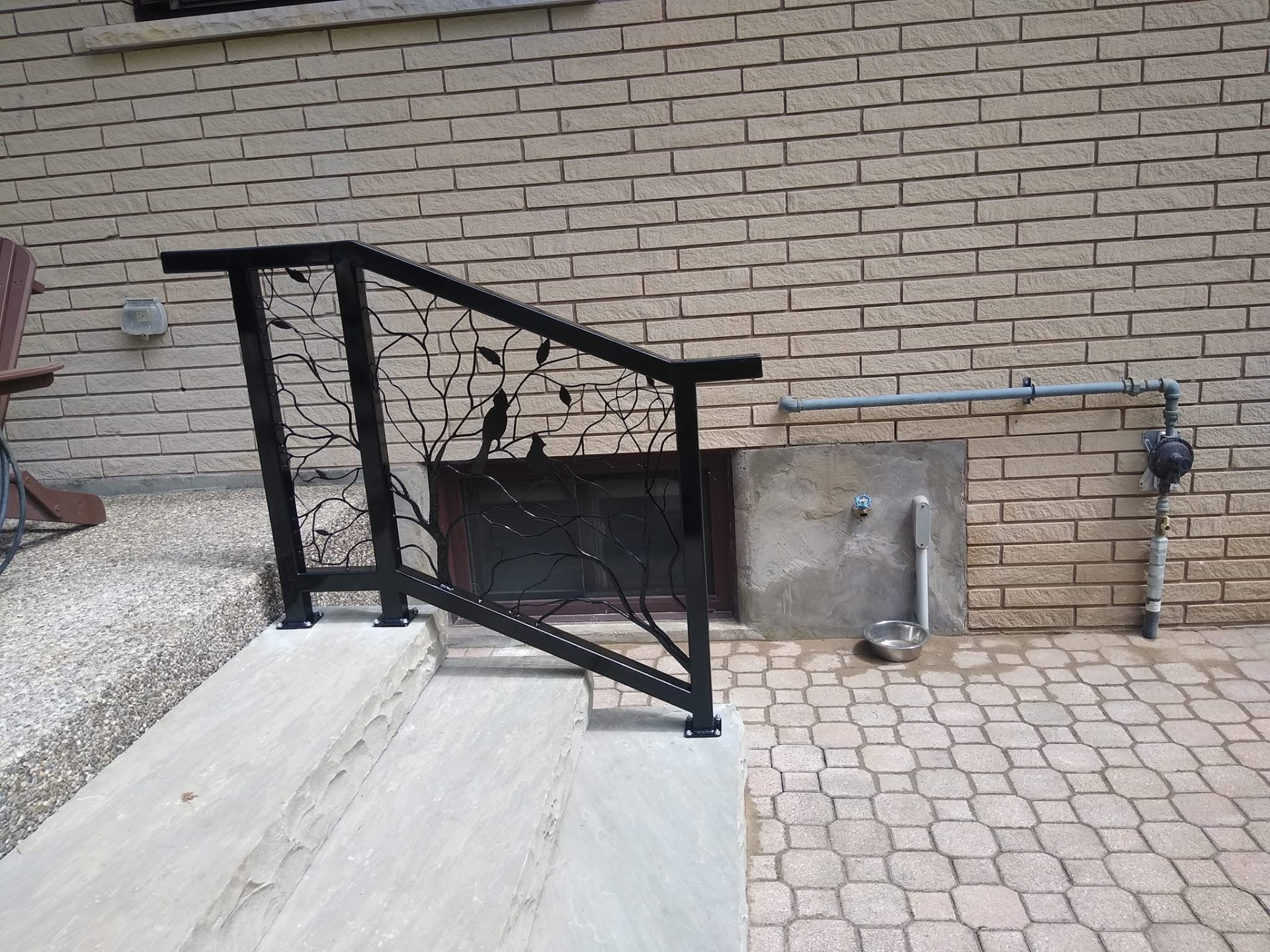 Decorative black metal railing with birds and branches against a brick wall